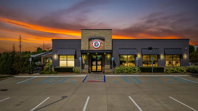 The Shelby Township restaurant under an orange sunset, windows glowing